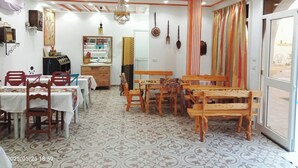 A dining area with wooden tables and chairs, a chandelier, and a patterned floor. - Dar Soulayma vacation home (Fatou houmet souk Djerba)