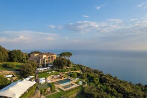 A coastal property with a swimming pool, a large villa, and a view of the sea.