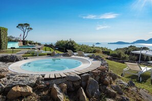 A hot tub surrounded by rocks and greenery, with a view of the sea and distant islands. - Golfo dei Poeti Relais & SPA (Ameglia)