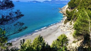 Un paisaje costero con una playa arenosa, mar azul cristalino y acantilados rocosos con pinos.