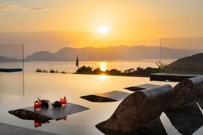 Ein Infinity-Pool mit Sonnenuntergangsblick, zwei Liegestühle und ein Tisch mit Getränken und einer Flagge.