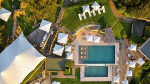 Vista aérea de un complejo turístico con piscina central, zonas de estar al aire libre y un jardín ajardinado.