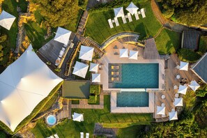 Vista aérea de un complejo turístico con piscina central, zonas de estar al aire libre y un jardín ajardinado.