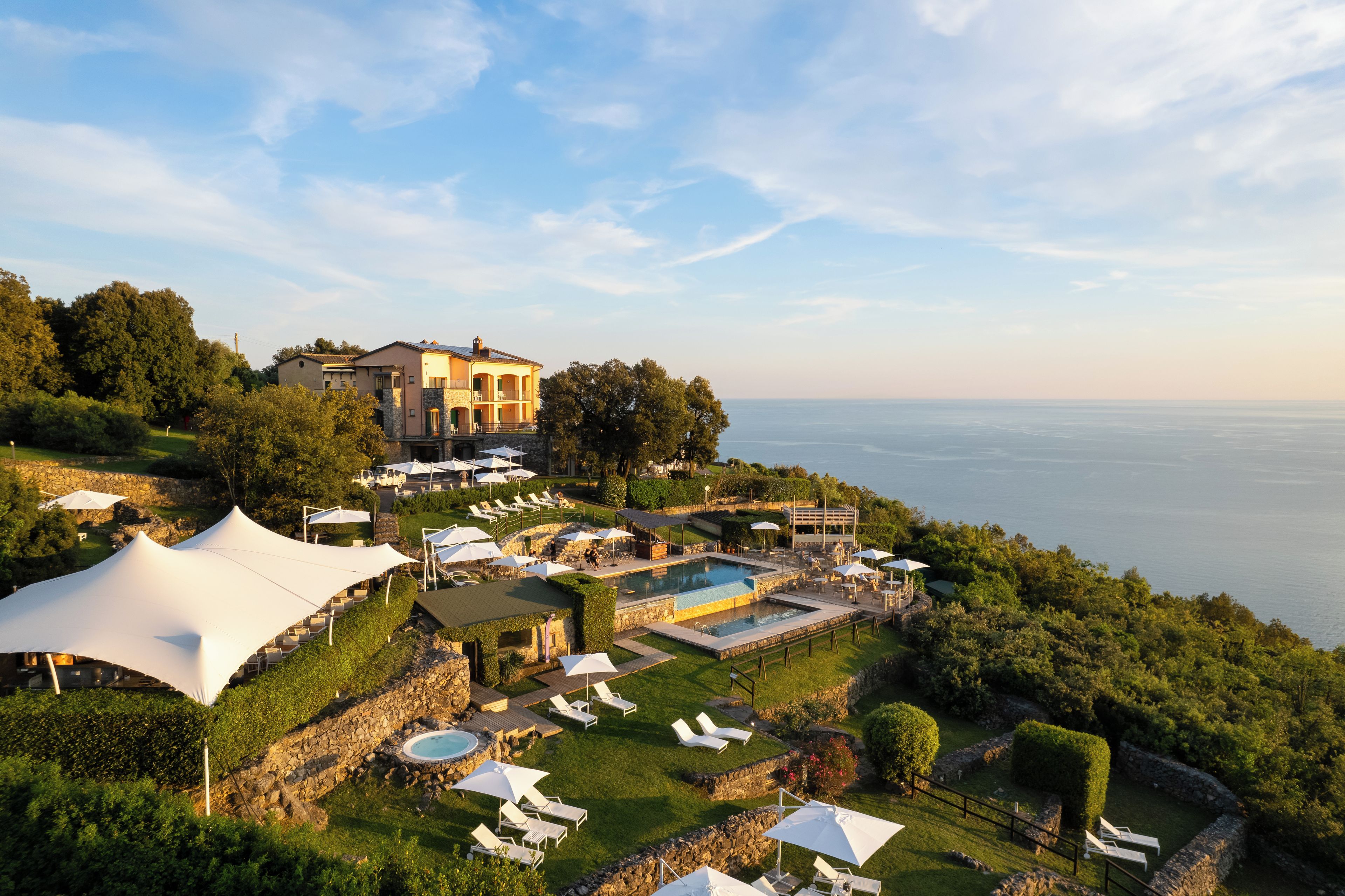 A resort with a large pool, multiple lounge areas, and a view of the sea.