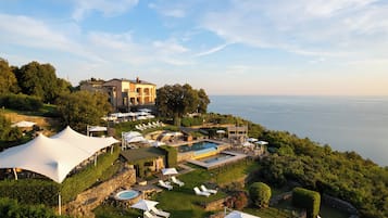 A resort with a large pool, multiple lounge areas, and a view of the sea.