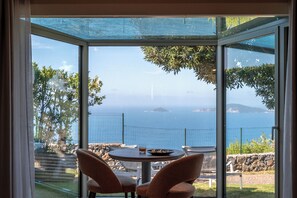 A glass-enclosed patio with a table and chairs, overlooking a scenic coastal view. - Golfo dei Poeti Relais & SPA (Ameglia)