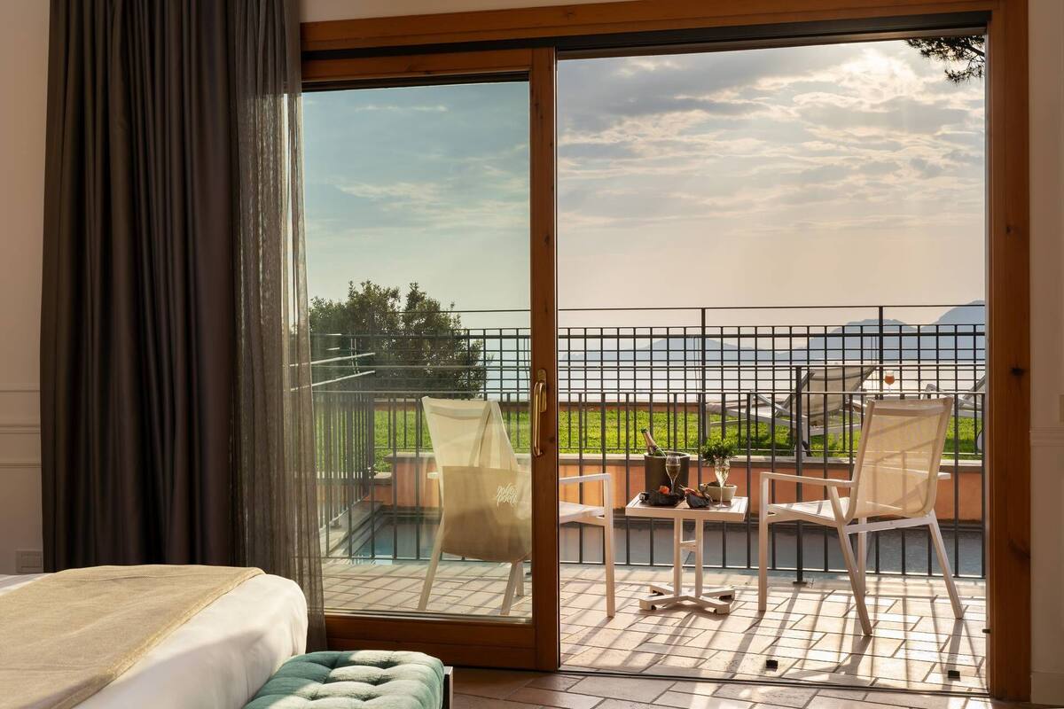 Une chambre d’hôtel dotée d’une grande porte-fenêtre coulissante donnant sur une terrasse extérieure avec vue sur la mer et les montagnes.