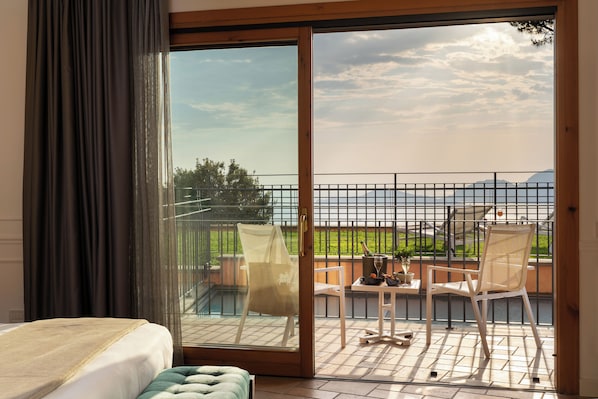 A hotel room with a sliding glass door leading to an outdoor balcony with a view of the sea and mountains.