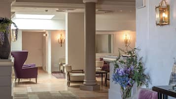 A spacious lobby with a high ceiling, a chandelier, and a seating area with chairs and a table.