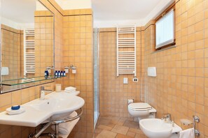 A modern bathroom with a large mirror, two sinks, a toilet, and a shower area.