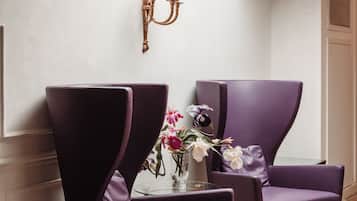 A room with two purple armchairs, a small table with a vase of flowers, and a wall-mounted candelabra.