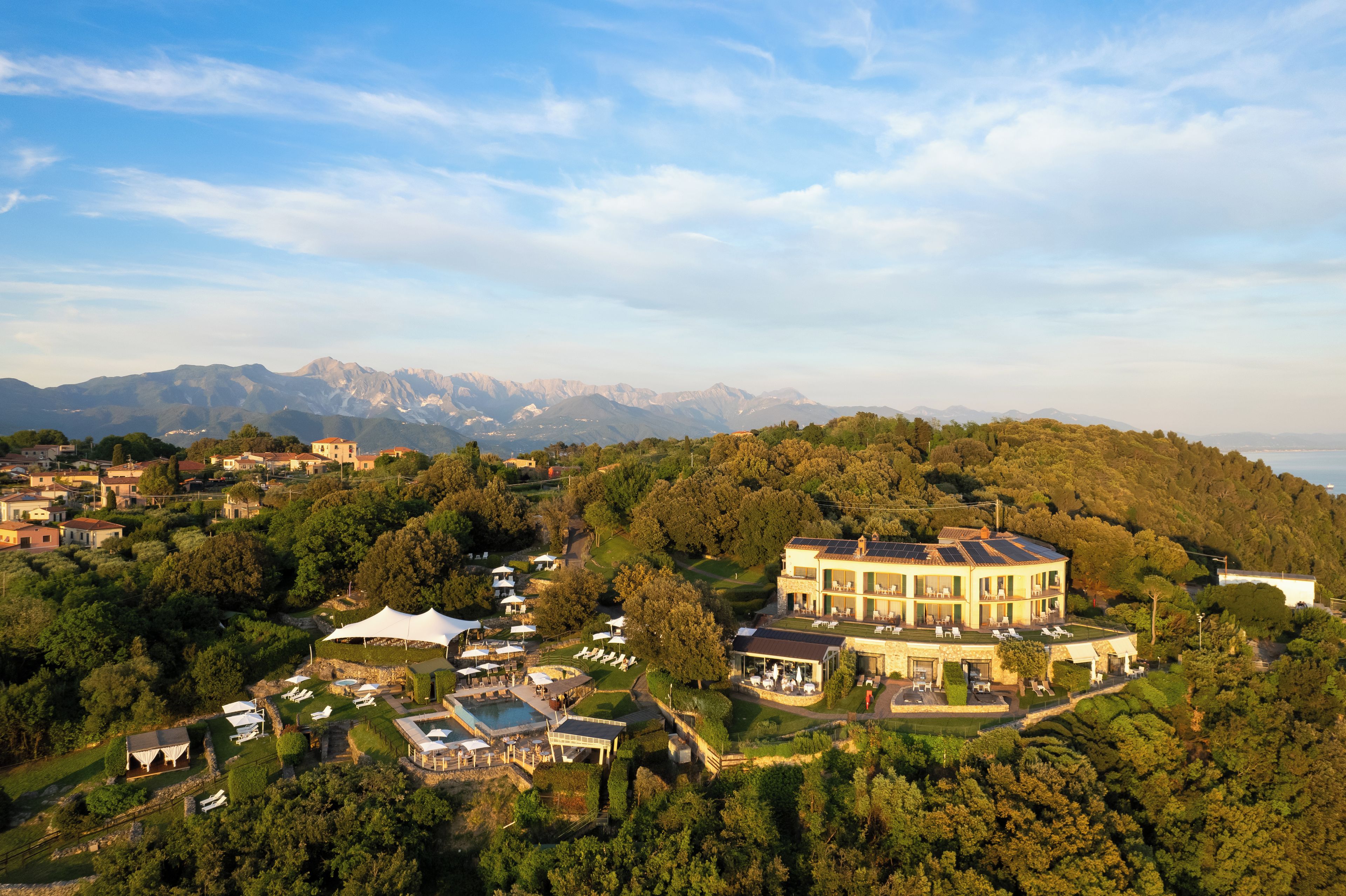 A large, multi-story building with a pool, surrounded by lush greenery and mountains in the background.