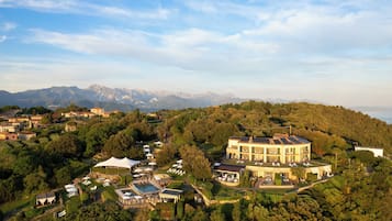 A large, multi-story building with a pool, surrounded by lush greenery and mountains in the background.