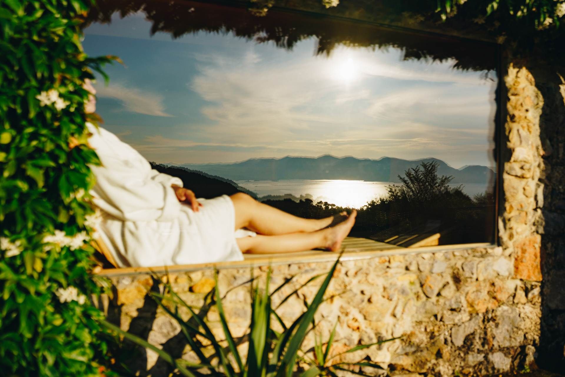 A person relaxing on a stone bench with a view of a lake and mountains.