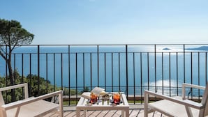 Un balcón con vistas despejadas al mar, dos sillas, una mesita con bebidas y un libro, y una barandilla metálica.
