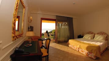 A hotel room with a bed, a desk with a telephone, a chair, a table with a lamp, and a view of the outdoors.