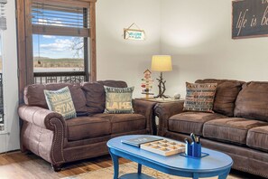Ein Wohnzimmer mit zwei braunen Ledersofas, einem blauen Couchtisch und einem Fenster mit Jalousien.
