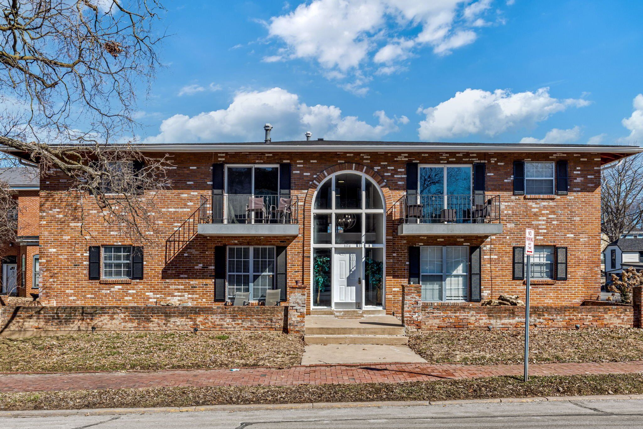 A two-story brick building with a central entrance, large windows, and a small balcony on the upper floor.