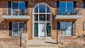 A two-story building with a brick facade, large arched windows, and a balcony with outdoor seating.
