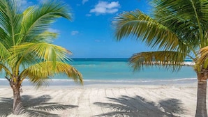Ein Sandstrand mit Palmen und wolkenlosem, blauem Himmel.