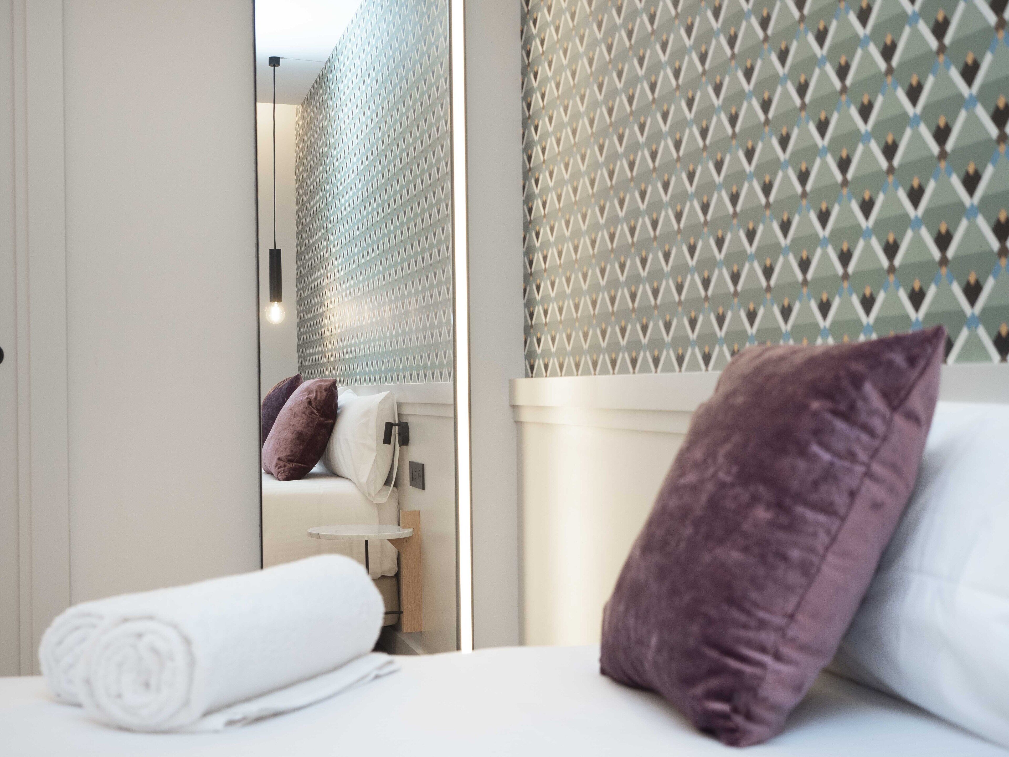 Una habitación de hotel con una cama, un baño visible a través de una puerta abierta y una pared con diseño.