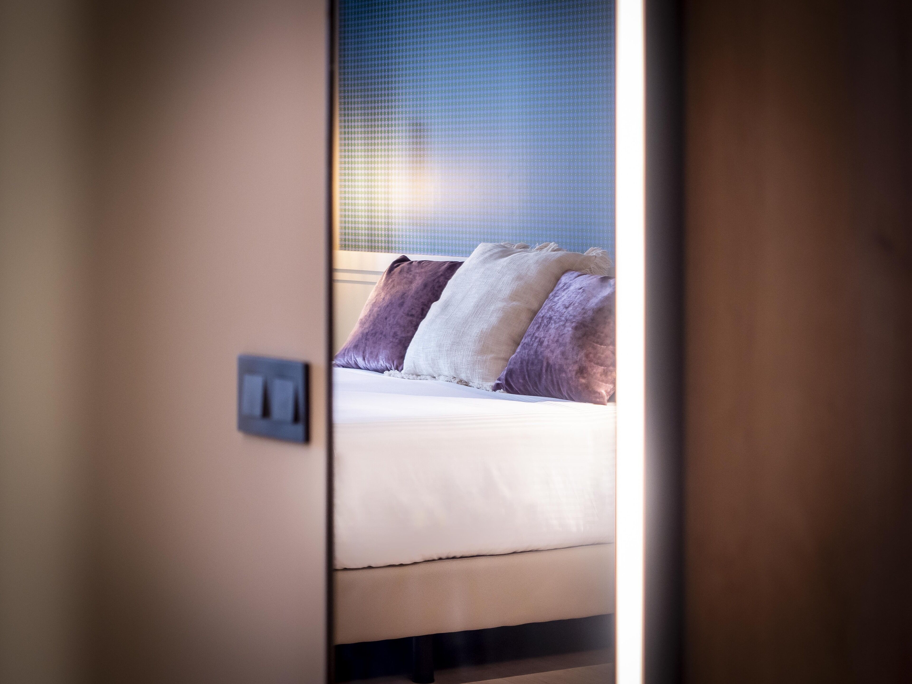 A hotel room with a bed, pillows, and a visible light switch on the wall.