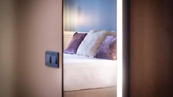 A hotel room with a bed, pillows, and a visible light switch on the wall.