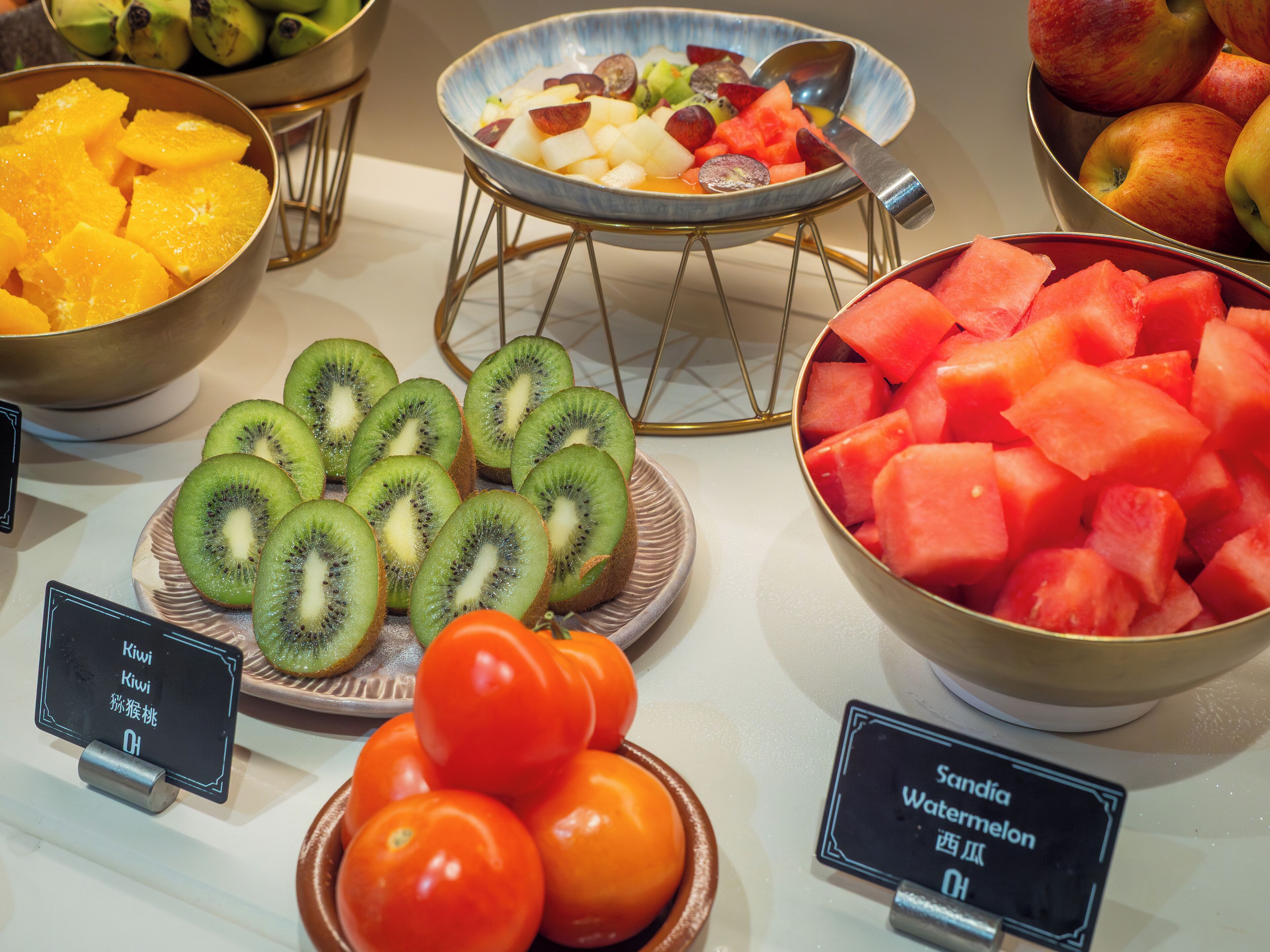Una exhibición de frutas con kiwis, tomates, sandía y otras frutas.