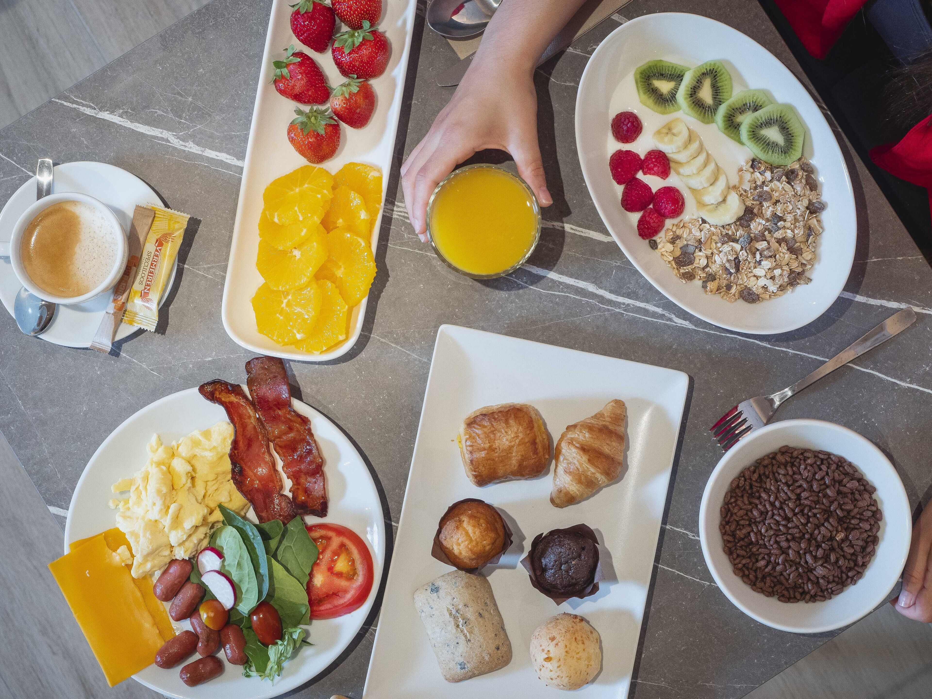 Un desayuno con una variedad de platillos, incluyendo huevos, tocino, tostadas y frutas.