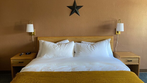 A hotel room with a wooden headboard, white bedding, a star decoration on the wall, and bedside lamps. - The Benson Motel - Benson, MN - US-12 HWY (Benson)