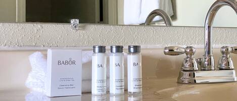 Un baño con espejo, lavamanos y tres productos de cuidado corporal Babolat.