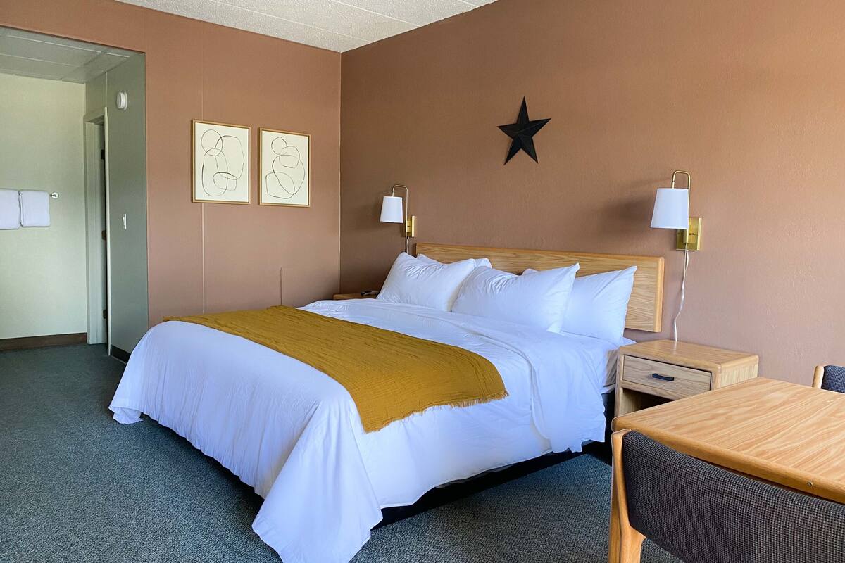 A hotel room with a bed, bedside tables, a desk, and a chair.