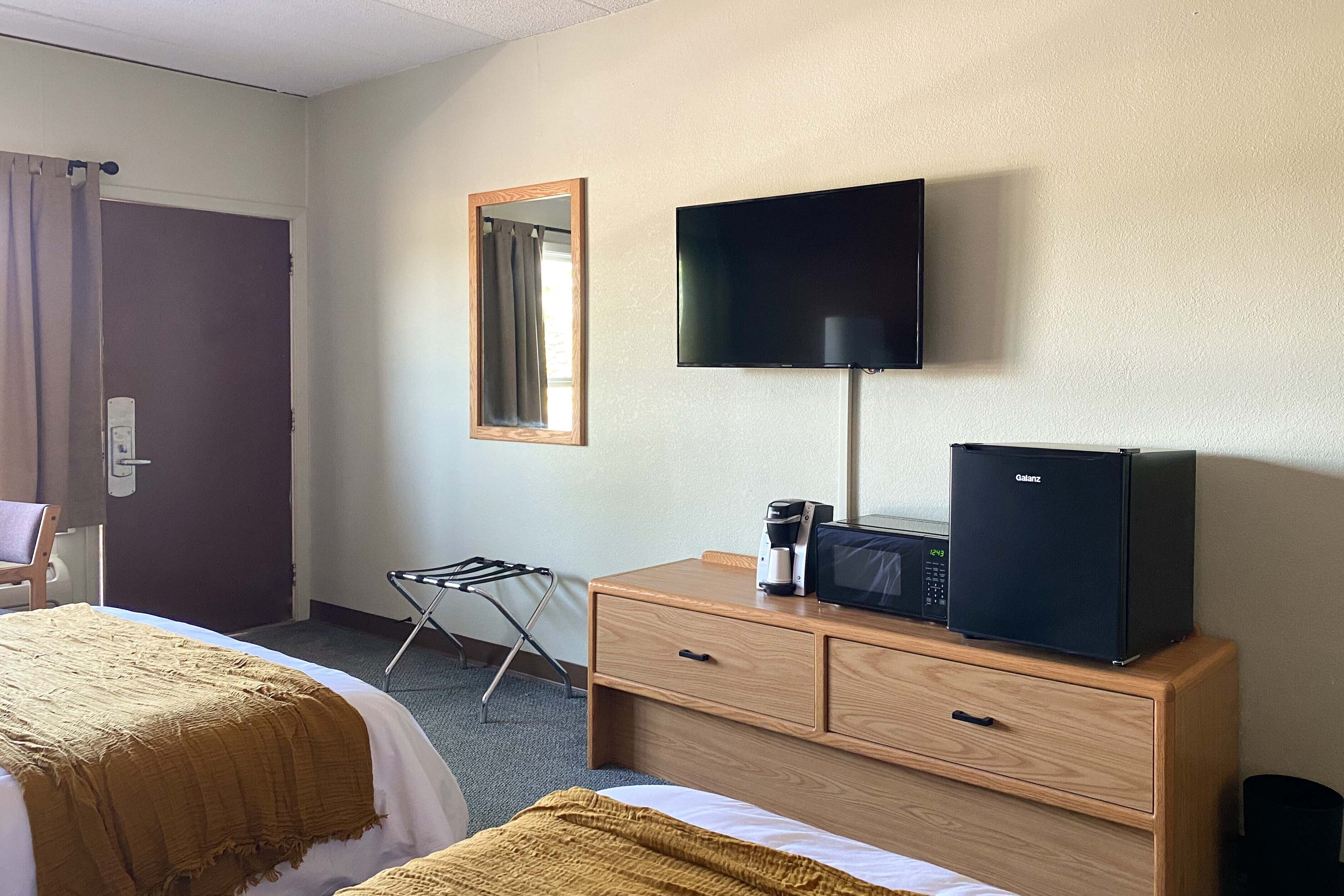 A hotel room with two beds, a flat-screen TV, a refrigerator, a microwave, a coffee maker, and a mirror.