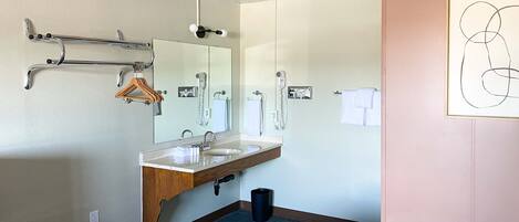 A hotel bathroom with a sink, mirror, towel rack, and a trash bin.