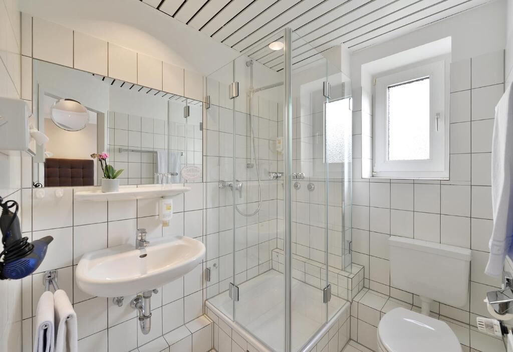 Un baño moderno con ducha de vidrio, lavamanos blanco y retrete.
