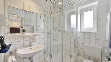 Un baño moderno con ducha de vidrio, lavamanos blanco y retrete.