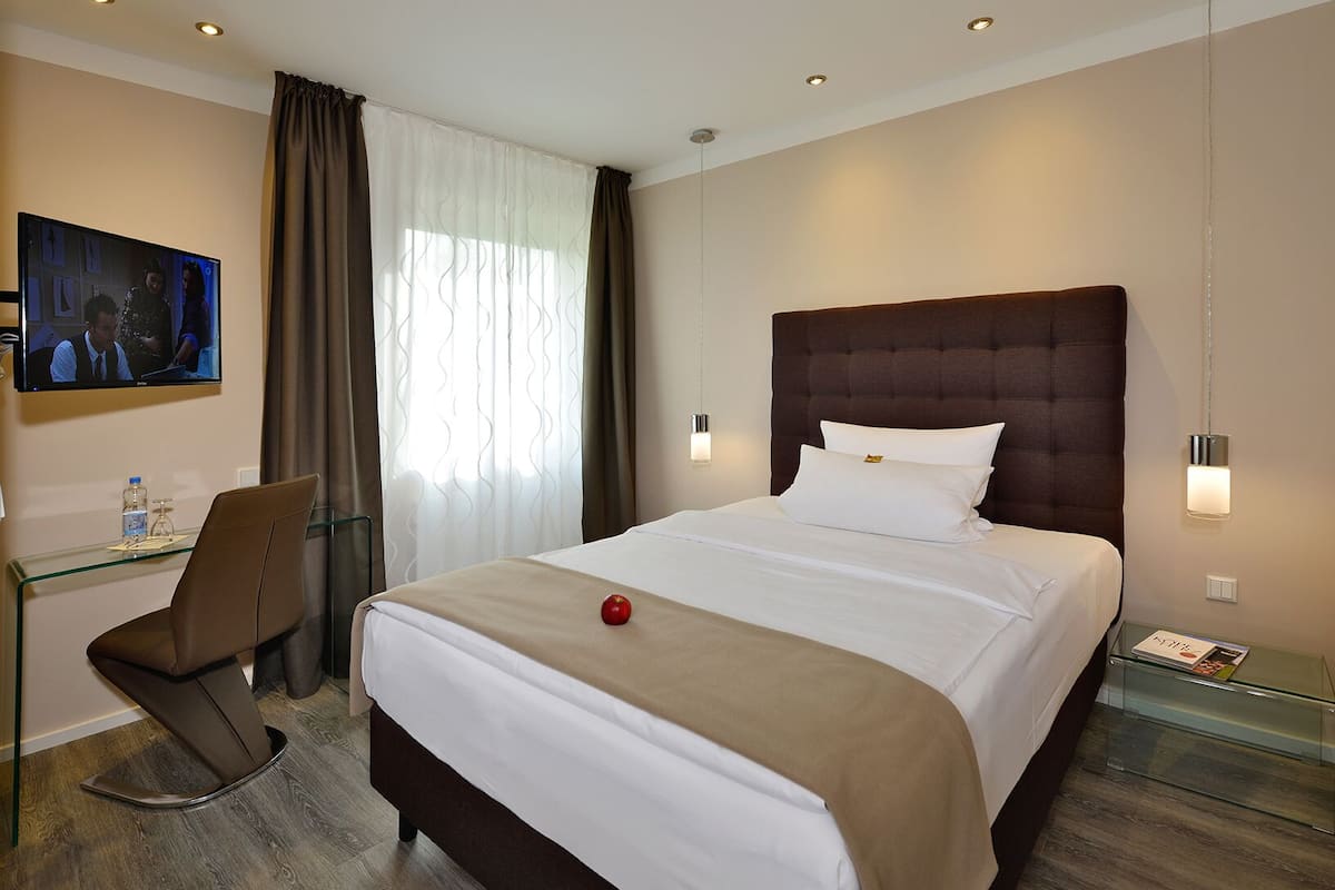 A hotel room with a bed, a desk, a chair, a television, and a window with curtains.