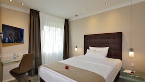 Ein Hotelzimmer mit Bett, Schreibtisch, Stuhl, Fernseher und einem fenster mit Vorhängen.