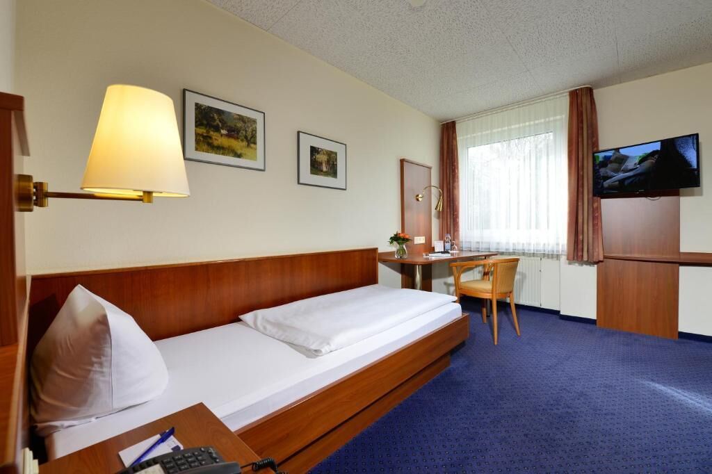A hotel room with a bed, desk, chair, TV, and two framed pictures on the wall.