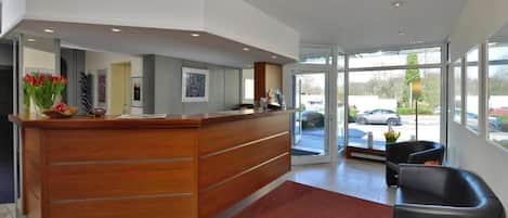 A reception area with a wooden desk, a red carpet, and black leather chairs.