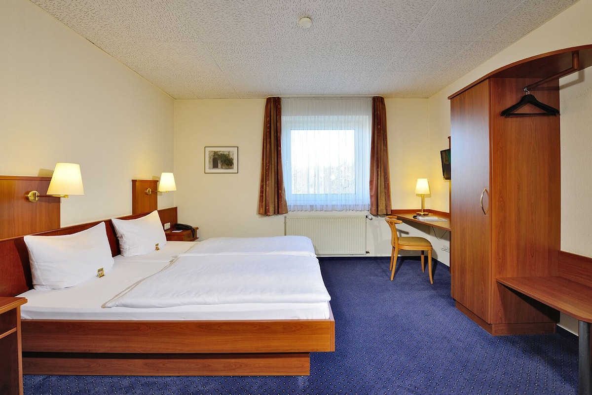 A hotel room with a large bed, two bedside tables with lamps, a desk with a chair, and a wardrobe.