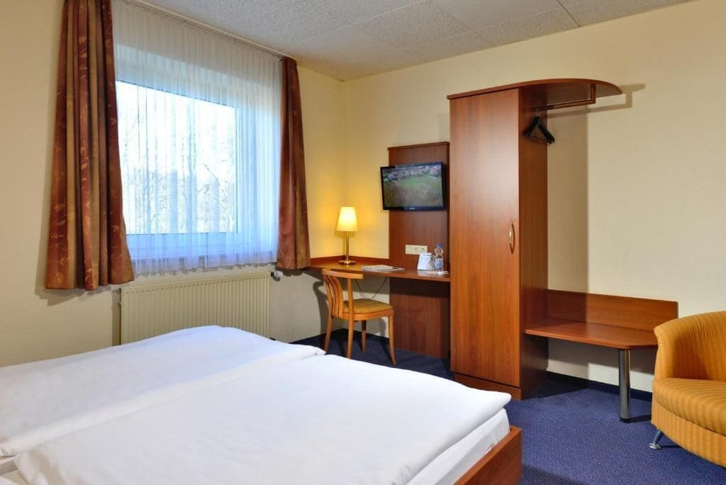 A hotel room with a bed, a desk with a chair, a television, and a wardrobe.