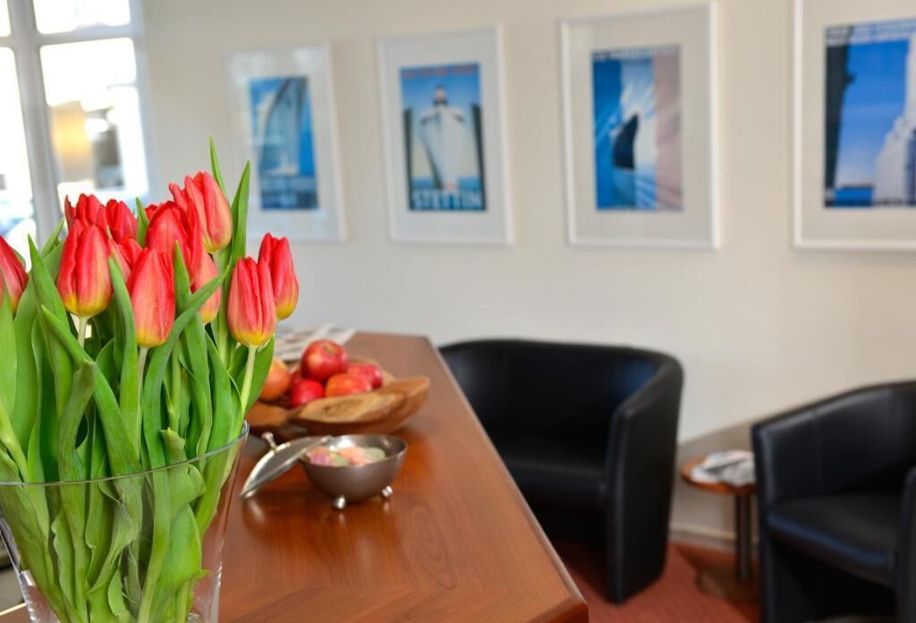 Una habitación con un escritorio de madera, un jarrón de tulipanes rojos, un frutero y cuadros en la pared.