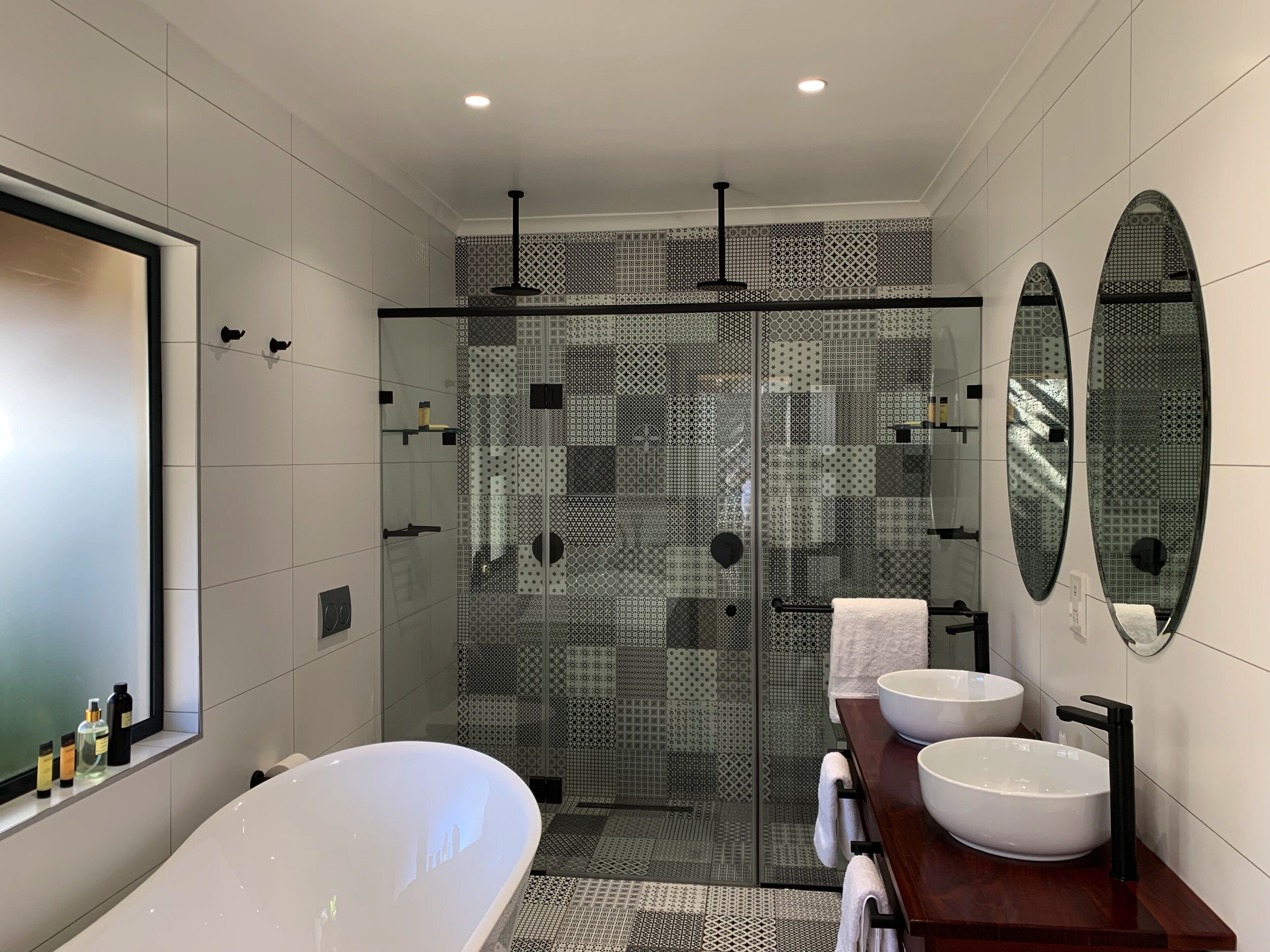 Un bagno moderno con una grande vasca, due lavabi e una doccia a filo pavimento con piastrelle decorate.