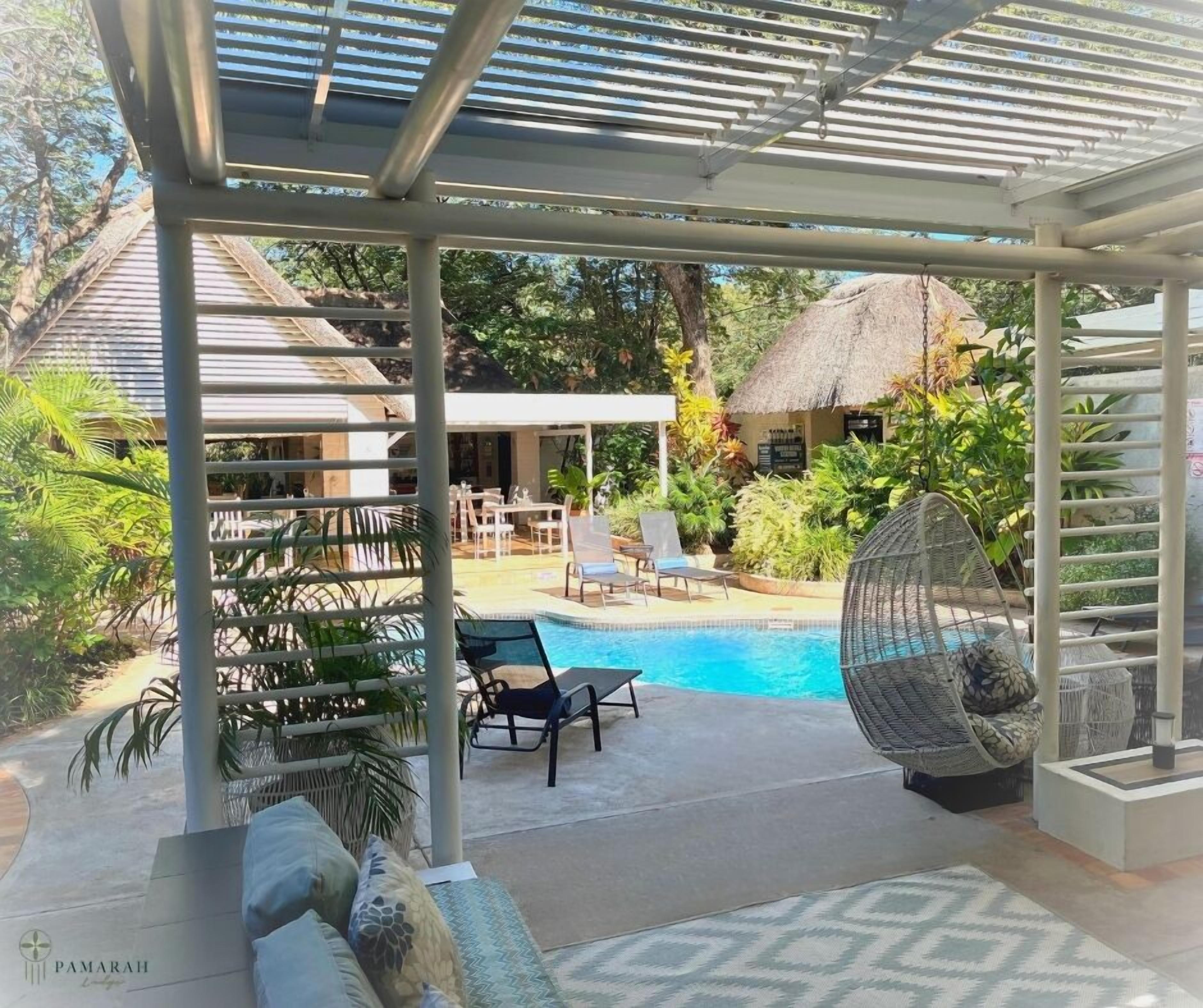 A covered outdoor area with a pool, lounge chairs, and a thatched-roof structure.
