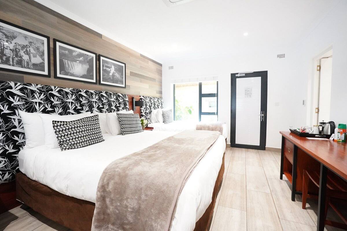 A modern hotel room with a large bed, a wooden headboard, and a desk with a coffee maker.