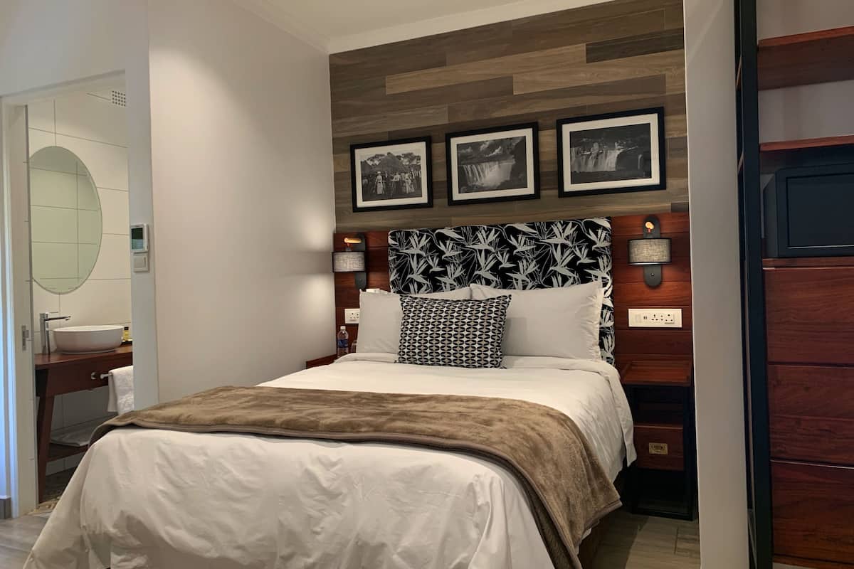 A hotel room with a large bed, a wooden headboard, and three framed pictures on the wall.