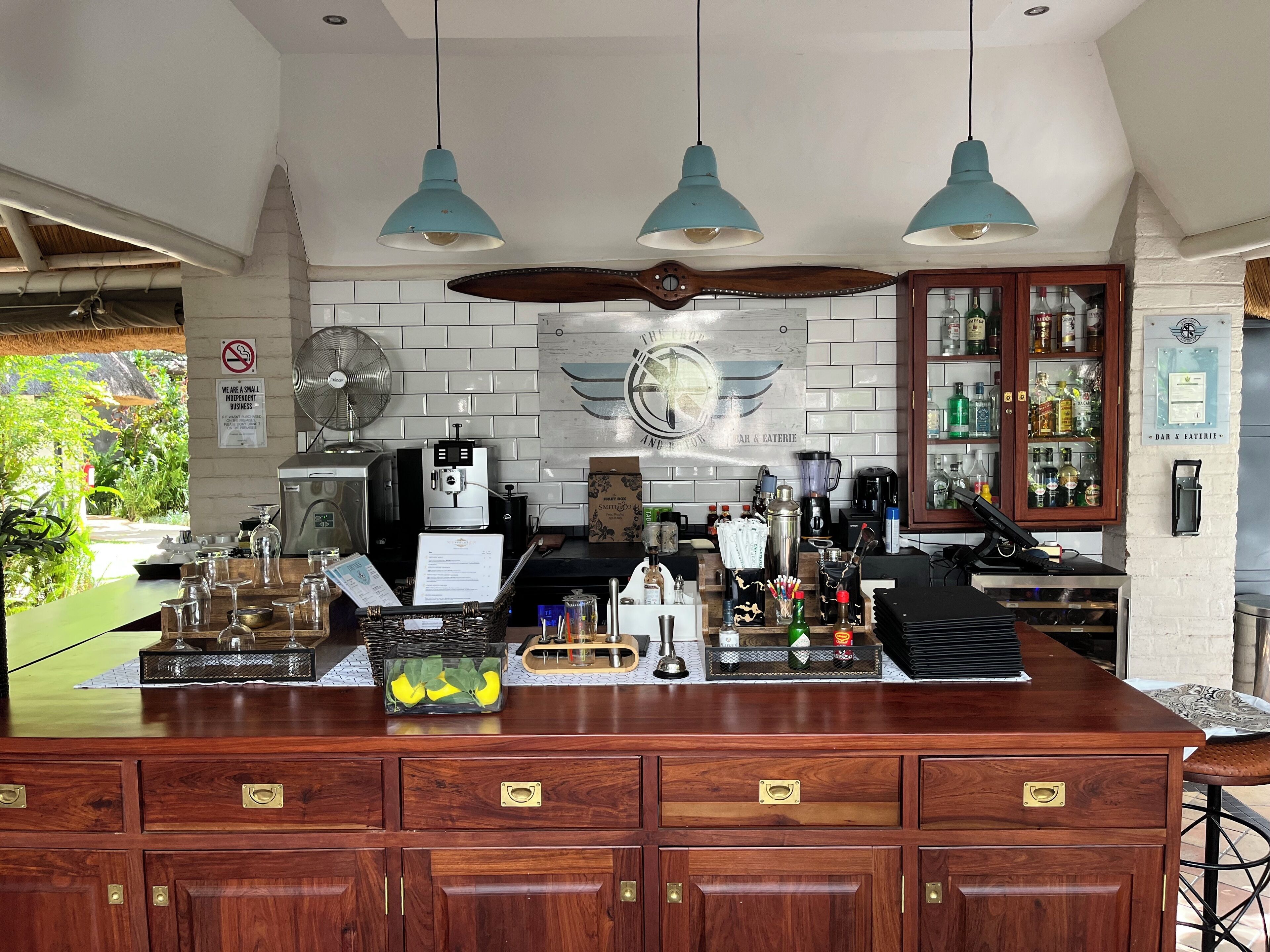 A bar area with a wooden counter, hanging blue pendant lights, a fan, and a sign indicating it's a small independent business.
