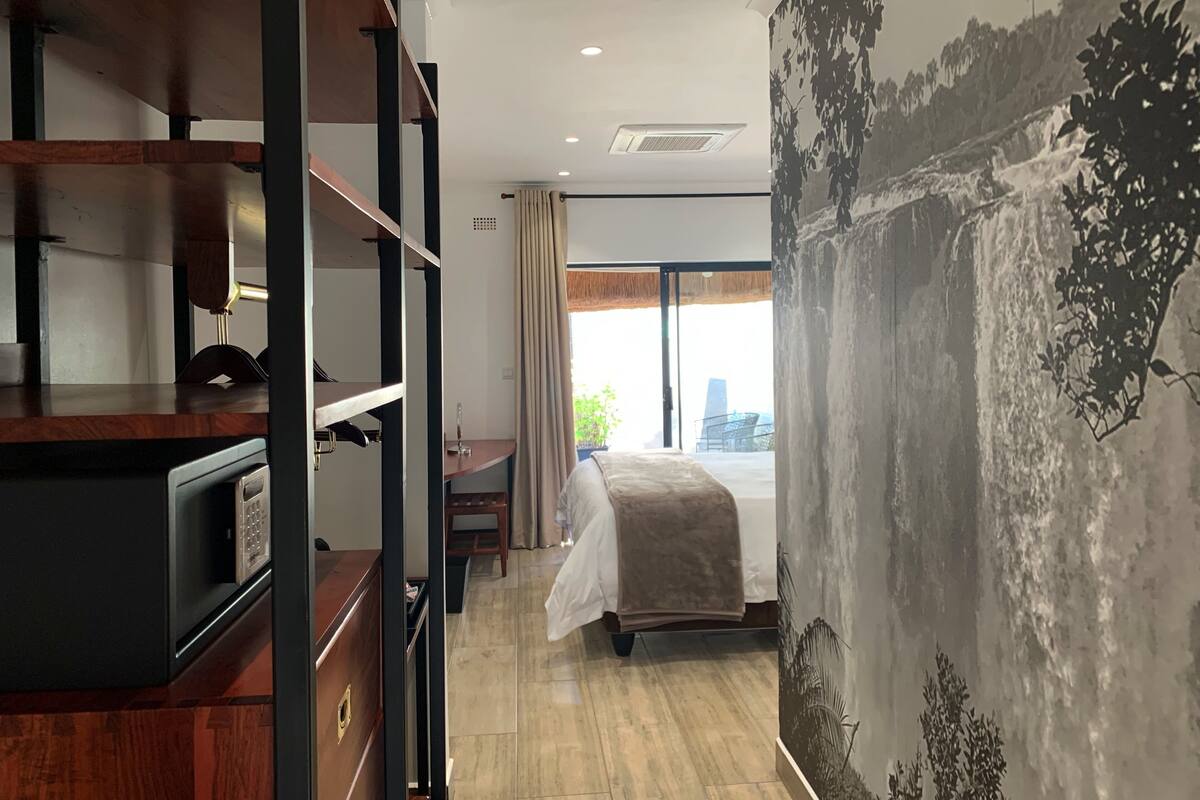 A hotel room with a bed, a desk, a wardrobe, and a large window with a view of a cityscape.