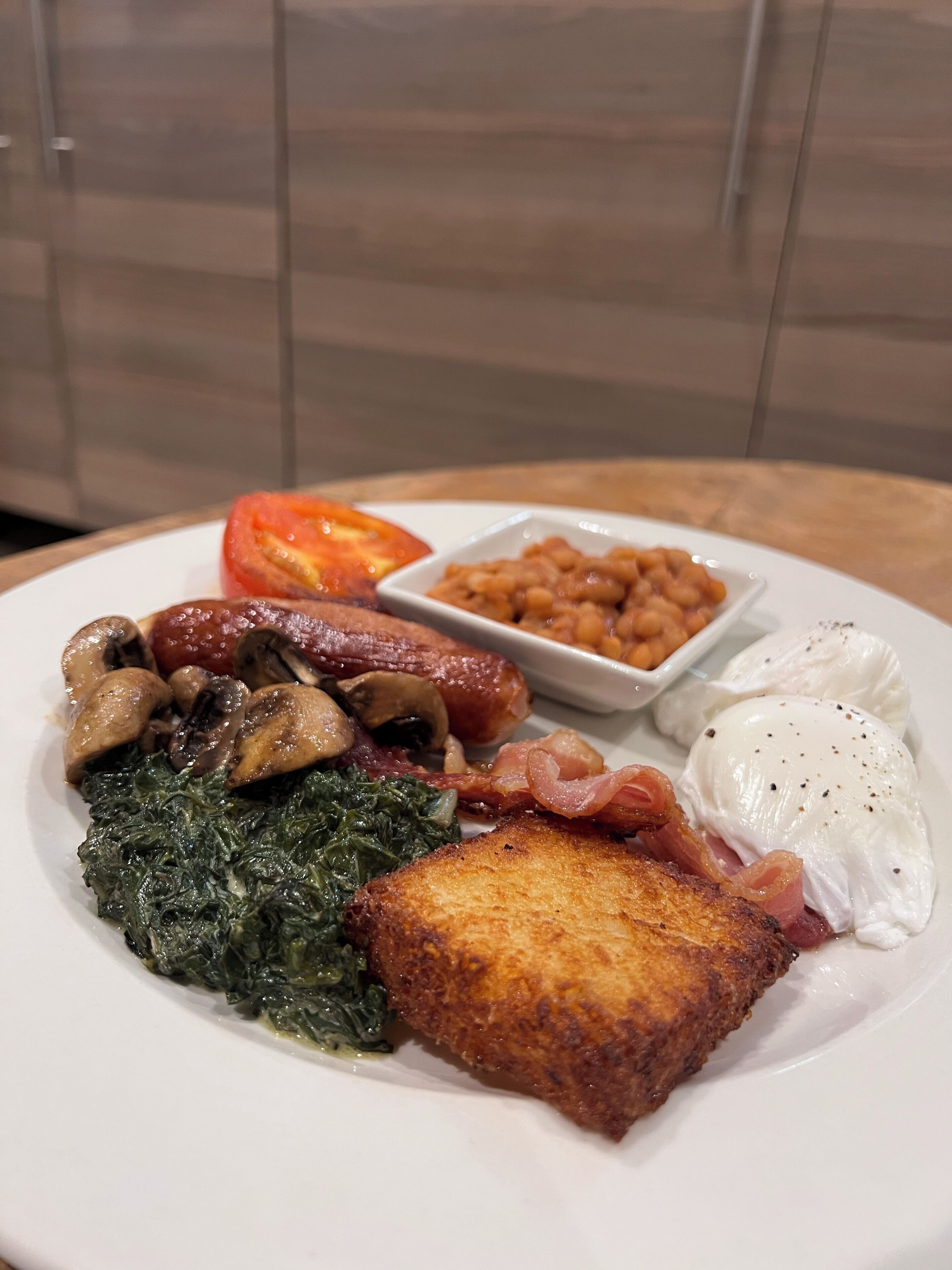 A plate of breakfast food including eggs, bacon, mushrooms, spinach, tomatoes, and beans.